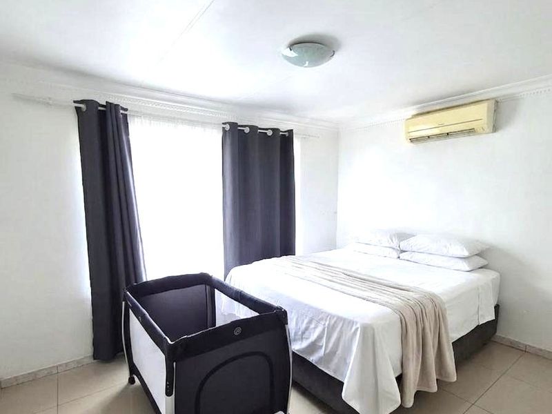 A bright bedroom featuring tiled flooring, crown molding, and a wall-mounted air conditioning unit.