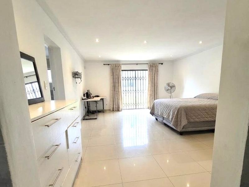 Spacious bedroom featuring large format floor tiles, recessed downlighting, and a sliding glass door with security gate leading to the exterior.