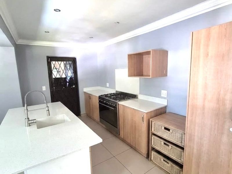 Modern kitchen featuring light wood cabinetry, stone countertops, a central island with a sink, and a built-in gas stove with an extractor.