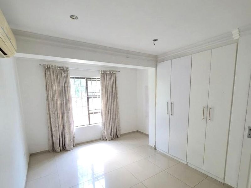 A bright, empty bedroom featuring large built-in wardrobes, tiled flooring, and a wall-mounted air conditioning unit.