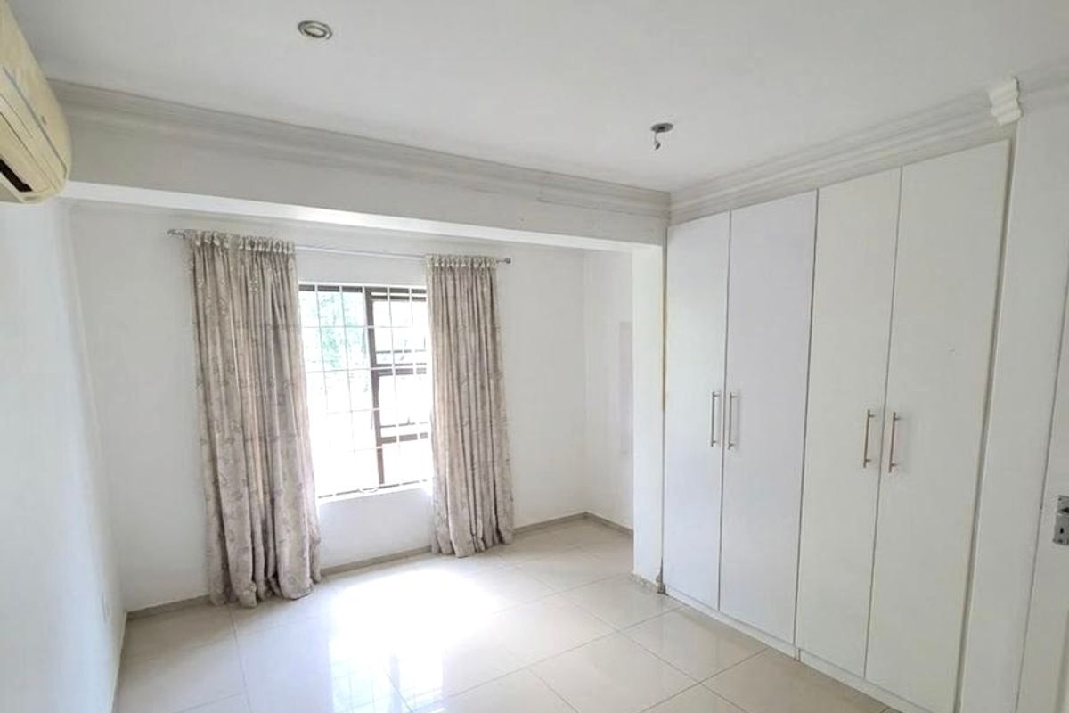 A bright, empty bedroom featuring large built-in wardrobes, tiled flooring, and a wall-mounted air conditioning unit.