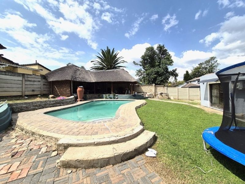 Outdoor pool area featuring a swimming pool with paved surround, a thatched lapa, and a grassed garden space.
