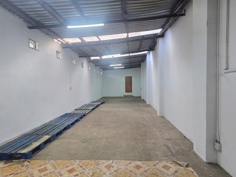 A spacious, empty utility or storage area featuring exposed roofing, concrete flooring, and basic electrical and plumbing infrastructure.