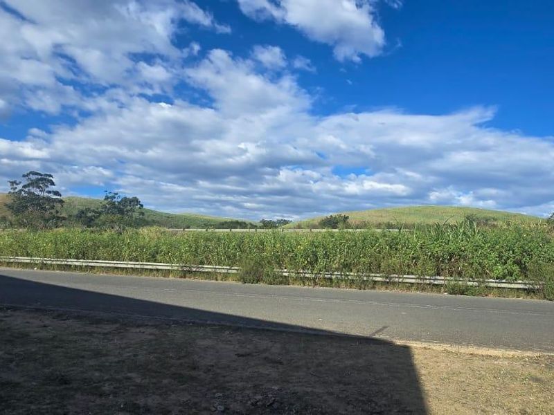 A view of the asphalt road and metal guardrail bordering the property, featuring open landscape and rolling hills in the background.
