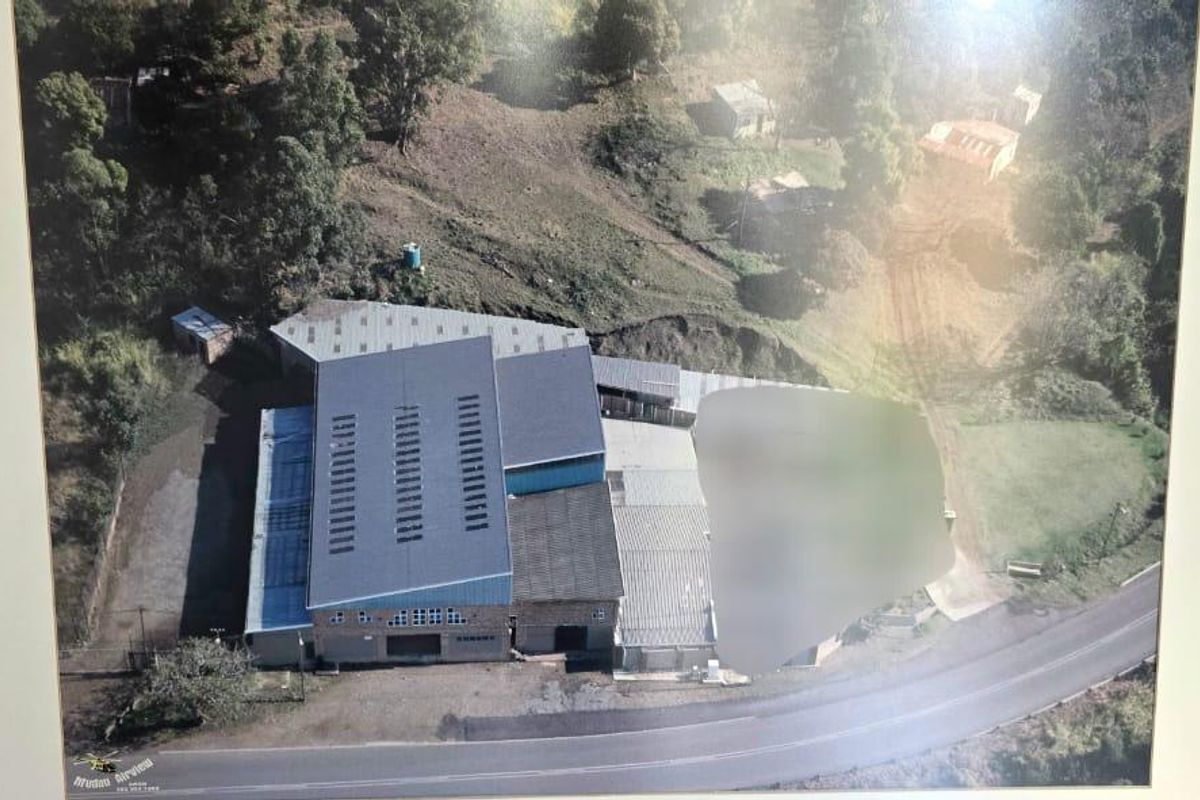 Aerial view of a commercial warehouse property with metal roofing, situated adjacent to a public road.