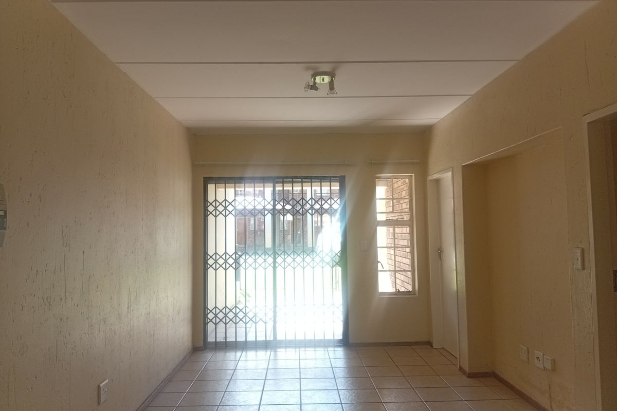 An empty living room featuring tiled flooring, a security gate, and a sliding door leading to an outdoor area.
