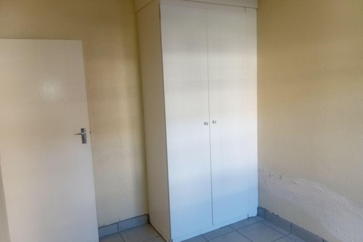 An empty bedroom featuring tiled flooring and a built-in cupboard, showing signs of wall surface wear and paint deterioration.
