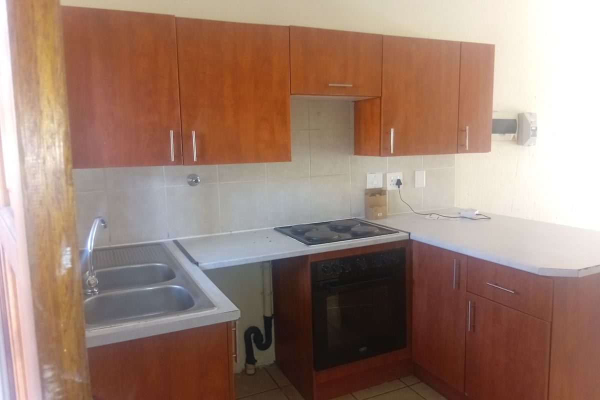 A functional kitchen featuring wood-look laminate cabinetry, a built-in electric oven with hob, double stainless steel sink, and tiled backsplash.