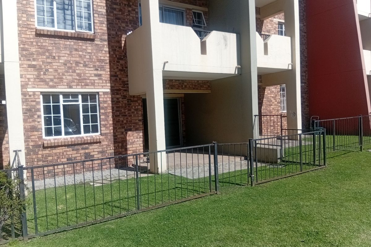 Ground floor apartment exterior featuring a brick facade, private paved patio area, and metal security fencing overlooking a communal lawn.