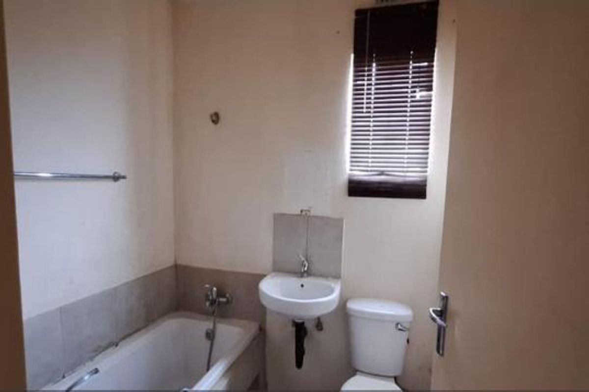 A functional bathroom featuring a bathtub, wall-mounted basin, and toilet, finished with neutral wall paint and a window blind.