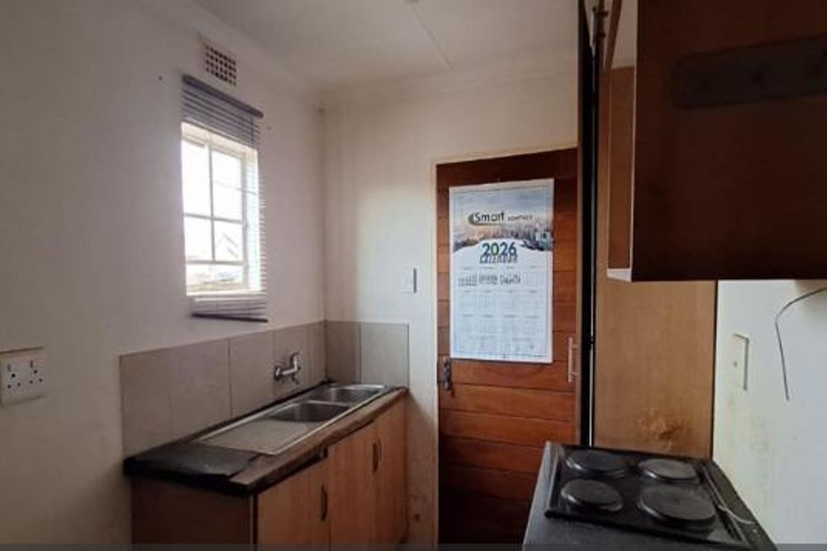 A compact kitchen featuring a double bowl sink, tiled splashback, and built-in cabinetry with an integrated electric hob.