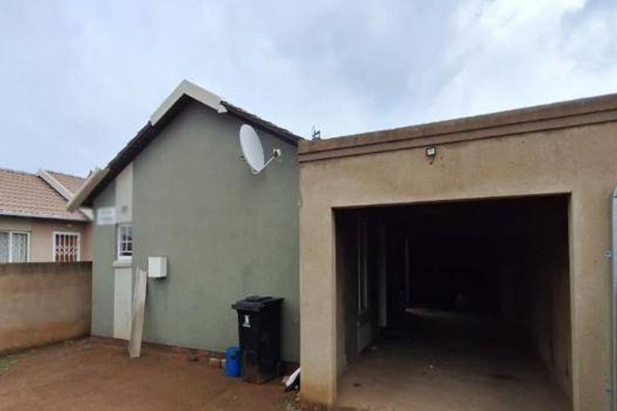 Rear view of the property featuring a single garage, boundary wall, and exterior wall with a mounted satellite dish.
