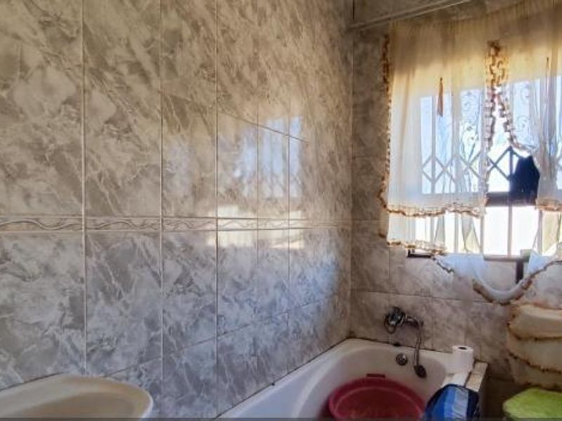 A functional bathroom featuring a bathtub, basin, and full-height marble-effect wall tiling with a security-fitted window.
