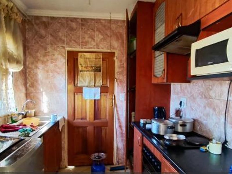A functional kitchen featuring wooden cabinetry, tiled splashbacks, and integrated appliances, offering a dated aesthetic with potential for modernization.