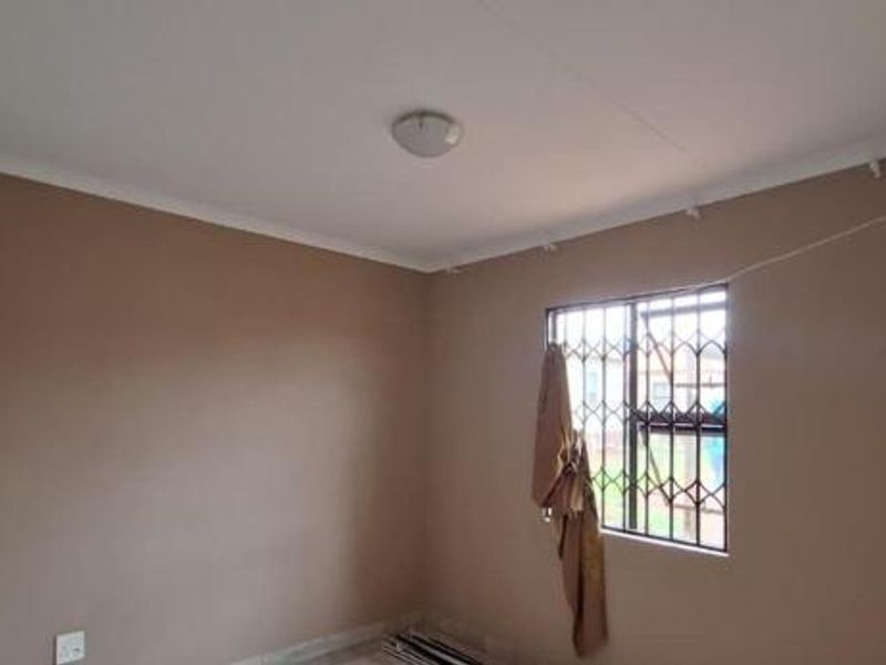 A clean, empty bedroom featuring neutral wall paint, a ceiling light fixture, and a window fitted with a security gate.