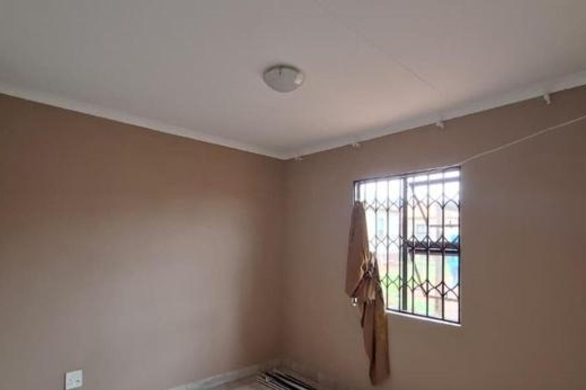 A clean, empty bedroom featuring neutral wall paint, a ceiling light fixture, and a window fitted with a security gate.