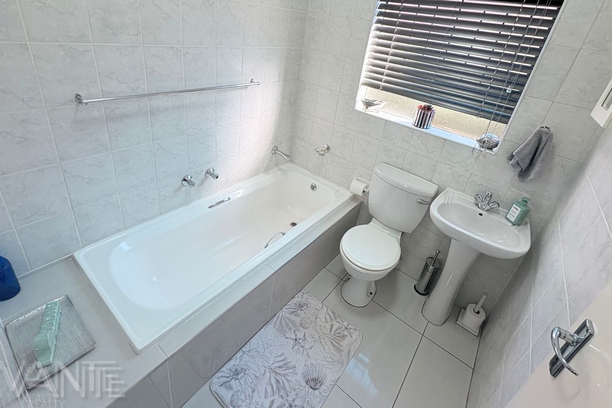 A clean, functional bathroom featuring a built-in bathtub, pedestal basin, toilet, and neutral tiled finishes throughout.