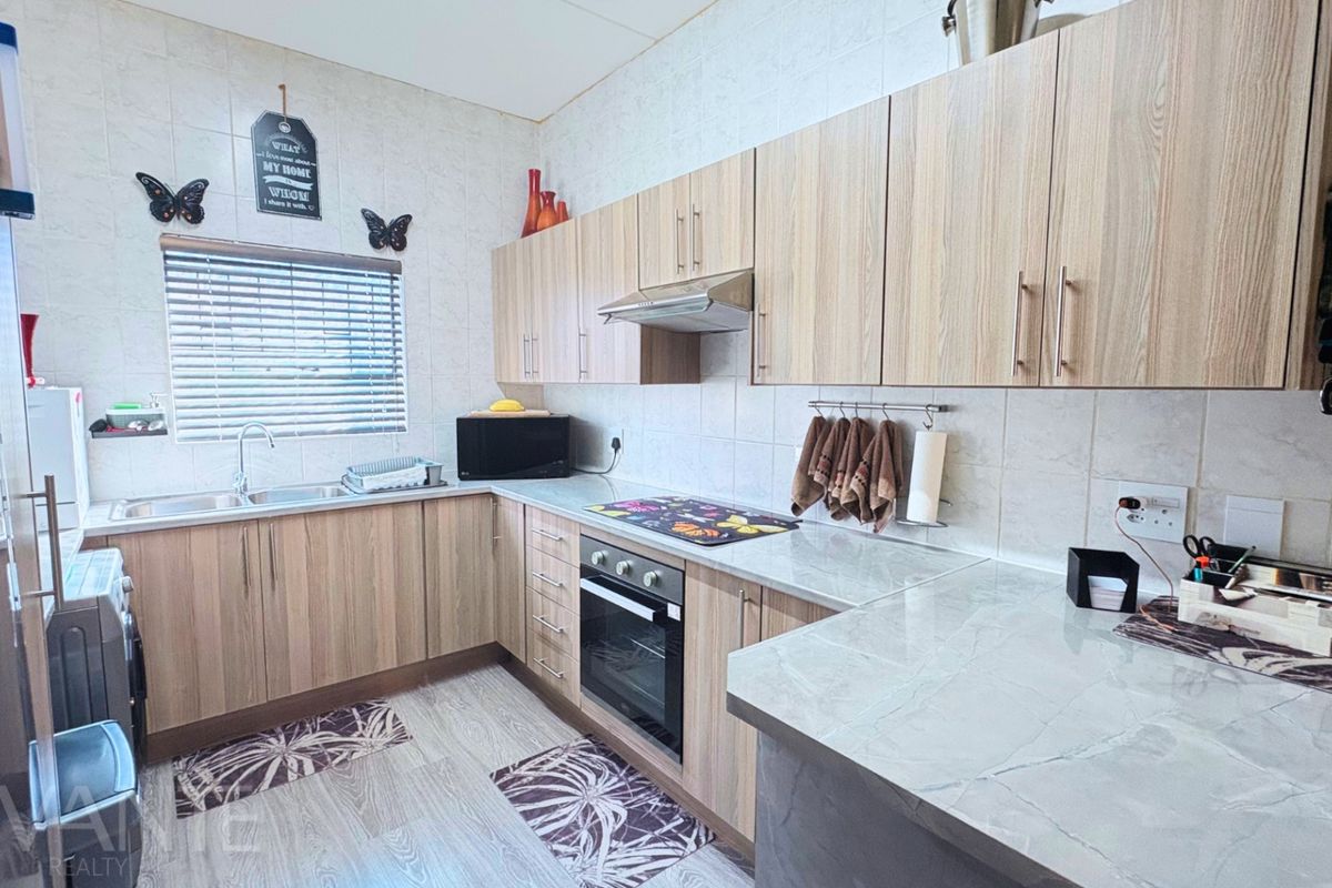 A functional kitchen featuring light wood-tone cabinetry, integrated oven and extractor fan, tiled backsplash, and ample counter space with a double sink.