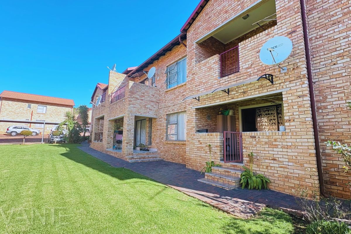 Rear view of a face brick apartment complex featuring ground floor paved patios and a well-maintained communal lawn area.