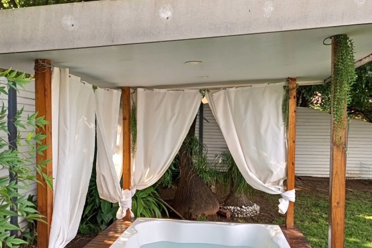 Outdoor garden area featuring a built-in jacuzzi set within a timber gazebo structure with a covered roof.