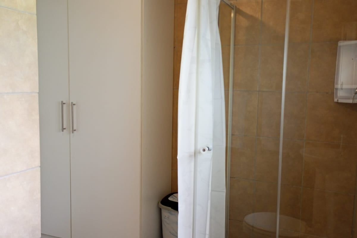 A functional bathroom featuring a shower enclosure, tiled finishes, and a built-in storage cupboard.
