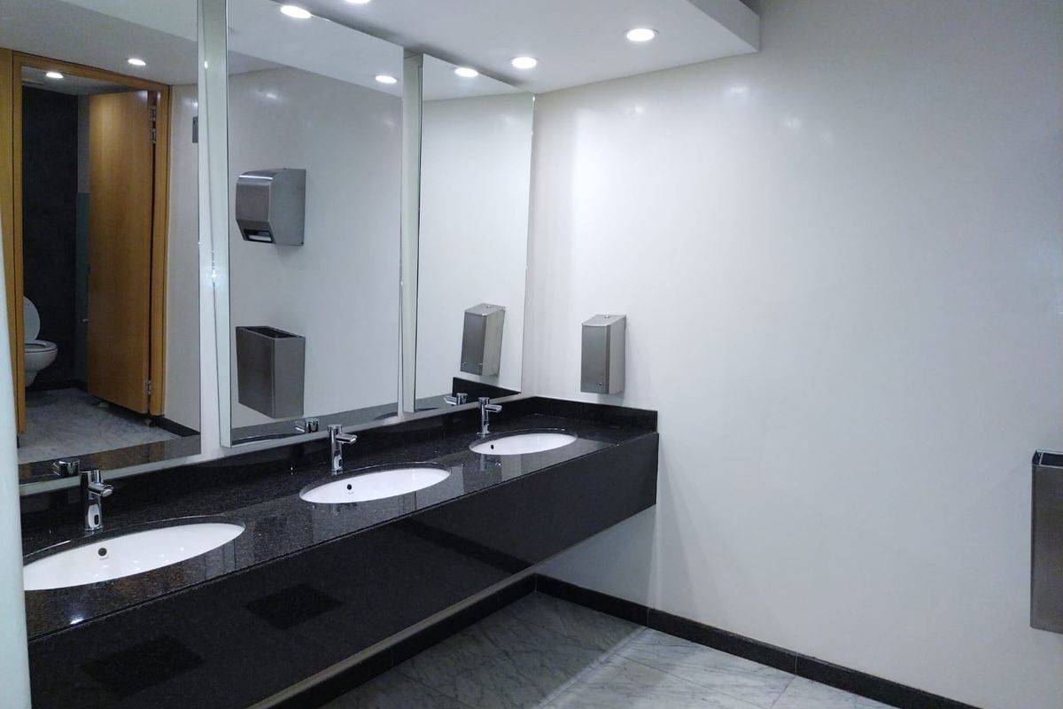 Modern commercial bathroom featuring a sleek granite vanity with triple undermount sinks, marble flooring, and integrated stainless steel fixtures.