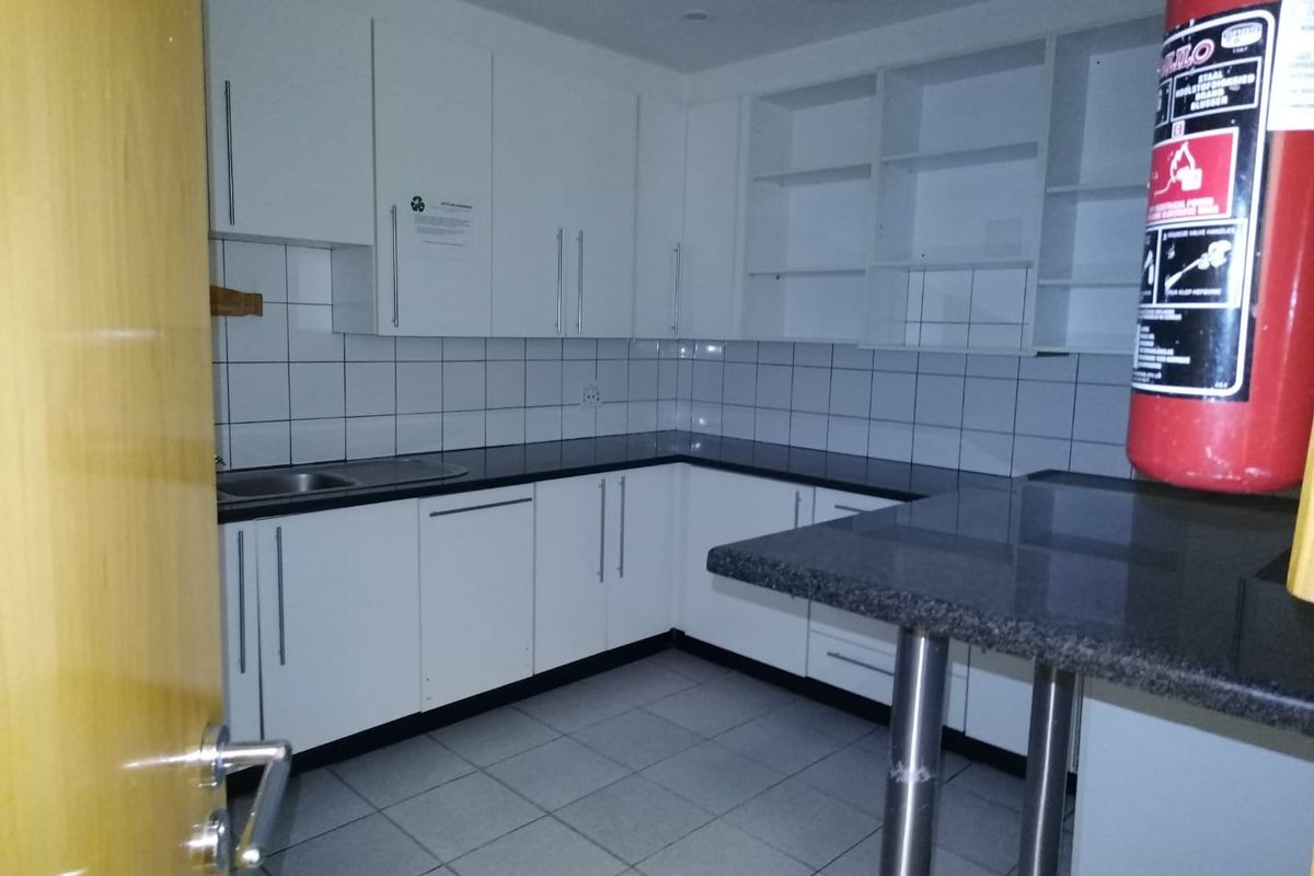 A clean, functional commercial kitchen space featuring white cabinetry, dark countertops, tiled backsplash, and ceramic flooring, suitable for office or staff use.