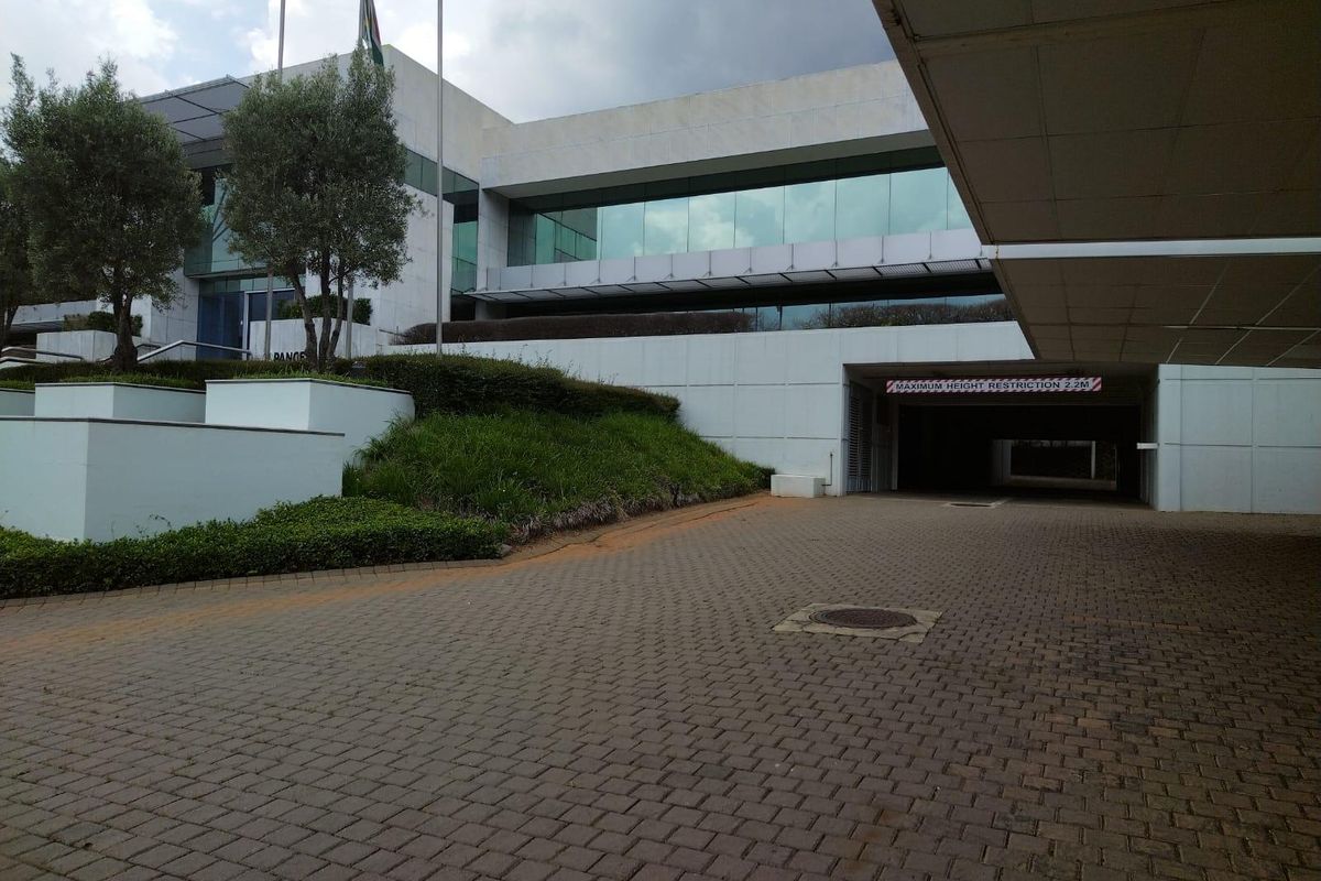 Front exterior view of a modern commercial building featuring a paved driveway, landscaped retaining walls, and a covered parking entrance.