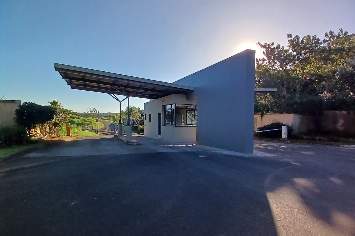 A modern residential estate security gatehouse featuring a cantilevered roof, asphalt driveway, and controlled access boom gate.