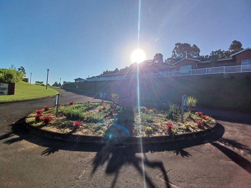 A view of the residential estate entrance featuring a landscaped roundabout, paved roads, and established street lighting under a clear sky.