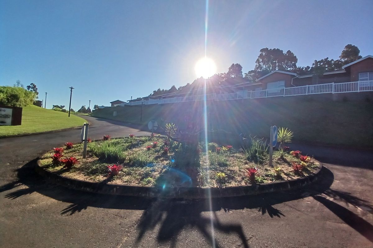 A view of the residential estate entrance featuring a landscaped roundabout, paved roads, and established street lighting under a clear sky.