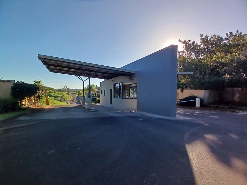 A modern residential estate security gatehouse featuring a cantilevered roof, asphalt driveway, and controlled access boom gate.