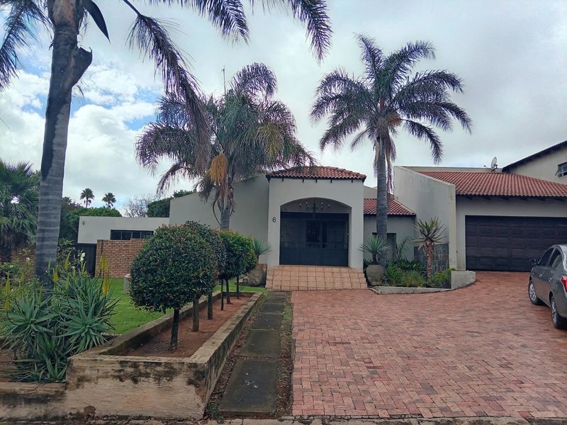 Front elevation of a residential property featuring a brick paved driveway, double garage, and a covered entrance porch with established garden landscaping.