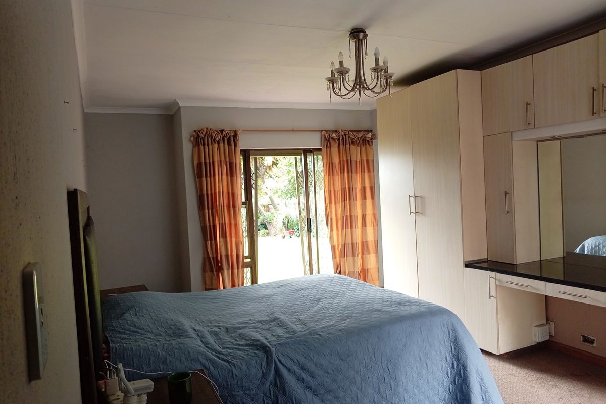 A bedroom featuring built-in cupboards, a vanity area, and a sliding glass door providing access to the garden.