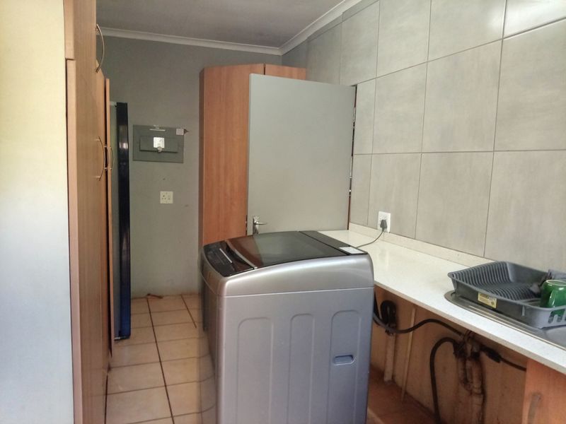 A functional laundry area featuring built-in cabinetry, tiled splashbacks, and a countertop with visible plumbing connections.