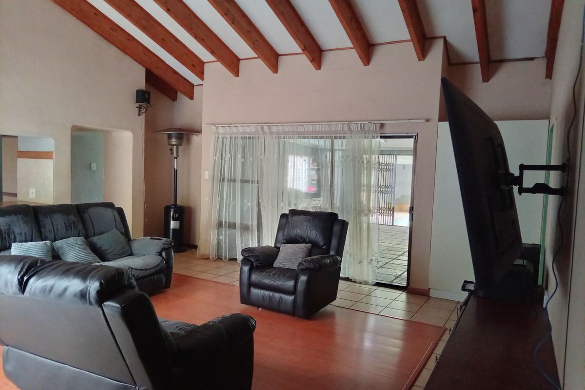 Spacious living room featuring high vaulted ceilings with exposed timber beams, tiled flooring, and large sliding glass doors providing access to the outdoor area.