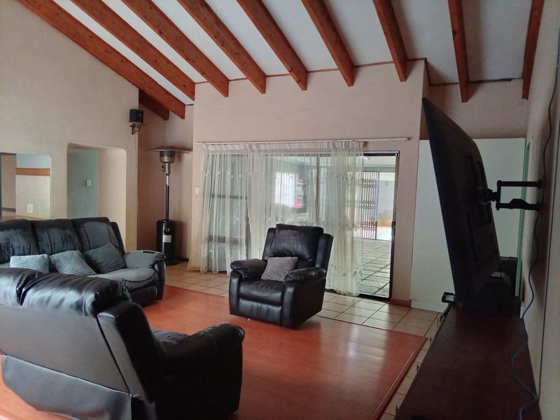 Spacious living room featuring high vaulted ceilings with exposed timber beams, tiled flooring, and large sliding glass doors providing access to the outdoor area.
