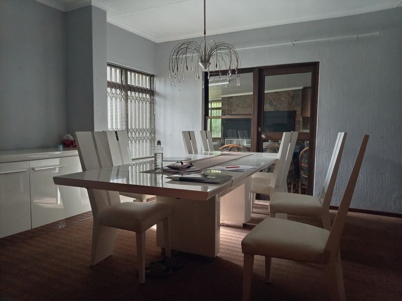 A dining room featuring built-in cabinetry, a sliding glass door with security gate, and a central pendant light fixture.