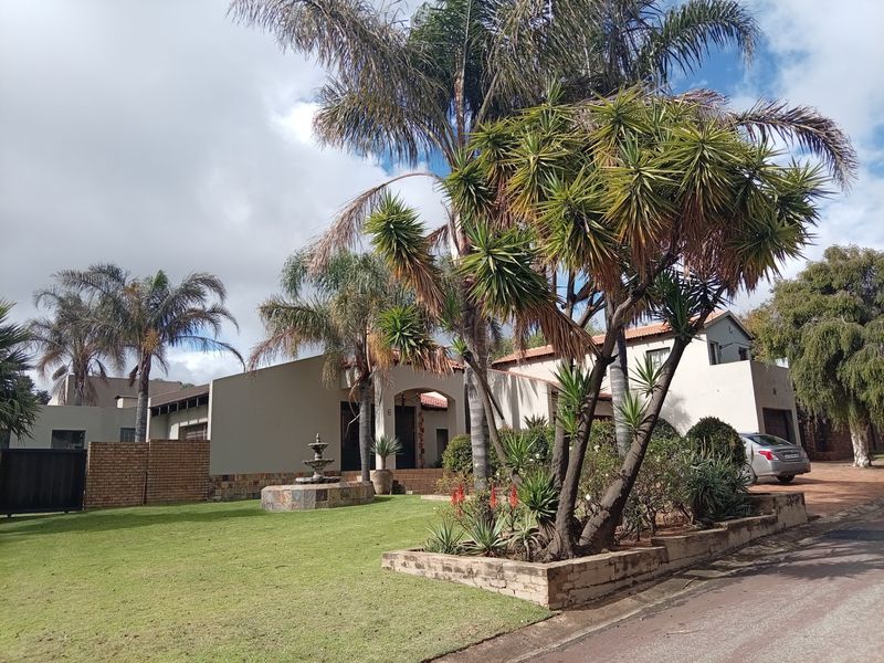 Front view of a residential property featuring a well-maintained garden, stone water fountain, paved driveway, and a classic plastered facade with tiled roofing.