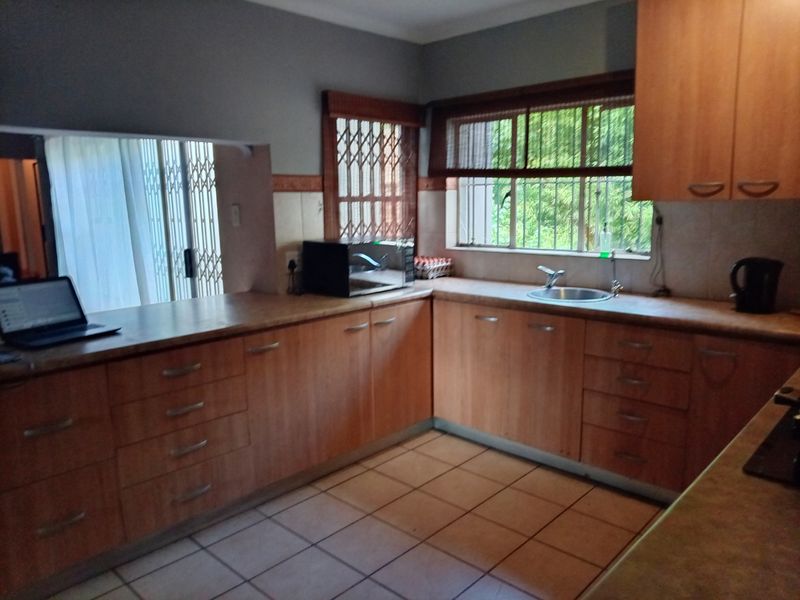 Functional kitchen featuring laminate cabinetry, ample countertop space, tiled flooring, and security gates on windows.
