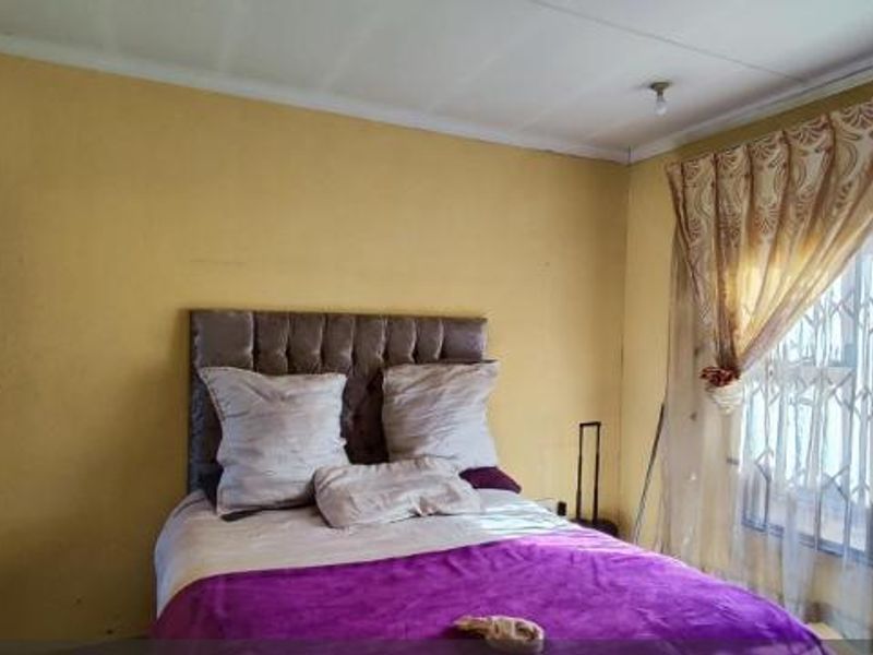 A bedroom featuring yellow painted walls, a window with security bars, and curtain rails.