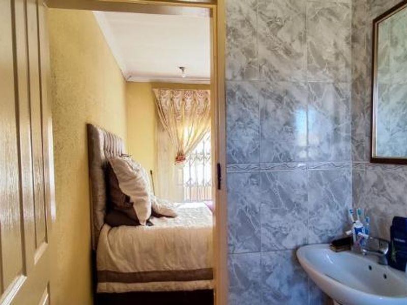 A compact bathroom featuring a pedestal washbasin and marble-effect wall tiling, with a view into the adjacent bedroom.