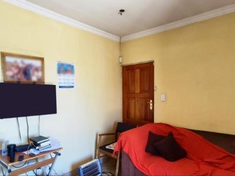A living room featuring a timber door and coving, currently requiring cosmetic updates to the wall finishes and lighting.
