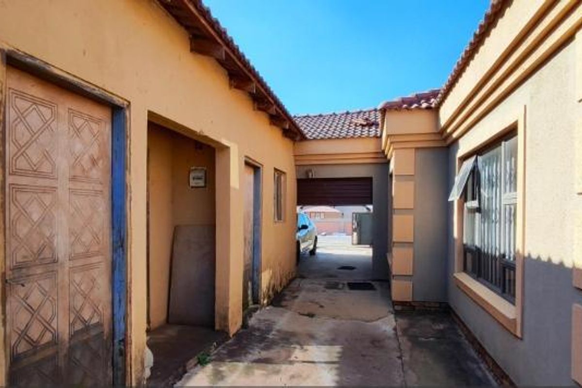 A view of the side passage and rear exterior area featuring concrete paving, security window bars, and weathered wall finishes.