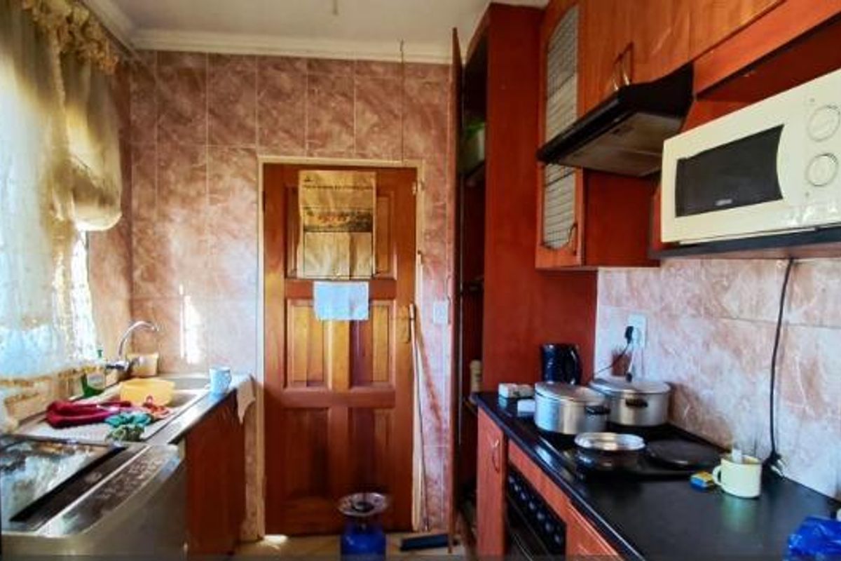 A functional kitchen featuring wooden cabinetry, tiled splashbacks, and integrated appliances, offering a dated aesthetic with potential for modernization.