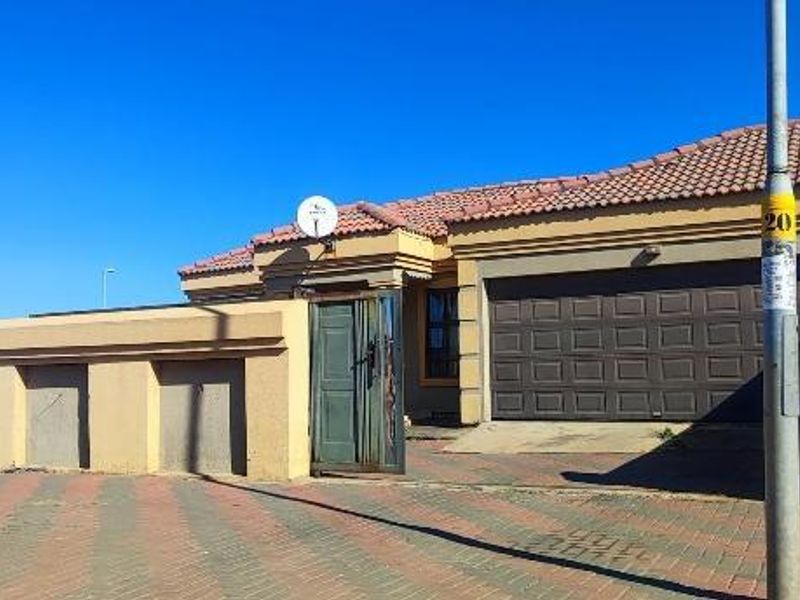 Front elevation of a single-story house featuring a tiled roof, paved driveway, and a secure garage with a boundary wall.