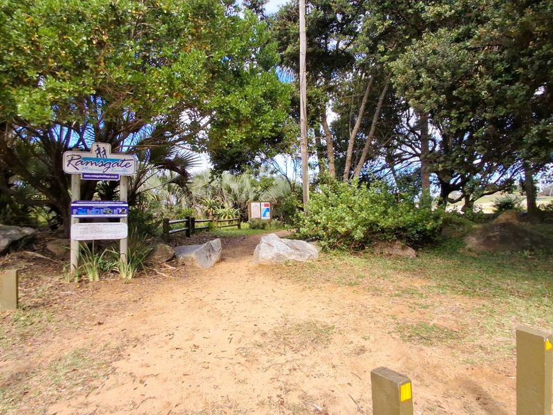 A natural, landscaped garden area featuring mature trees, wooden bollards, and local signage, providing a scenic outdoor space.