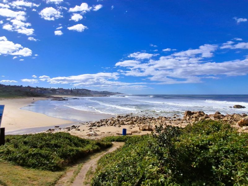 A scenic view of the coastline featuring a sandy beach, rocky shoreline, and ocean waves, highlighting the natural beauty of the vacant land location.