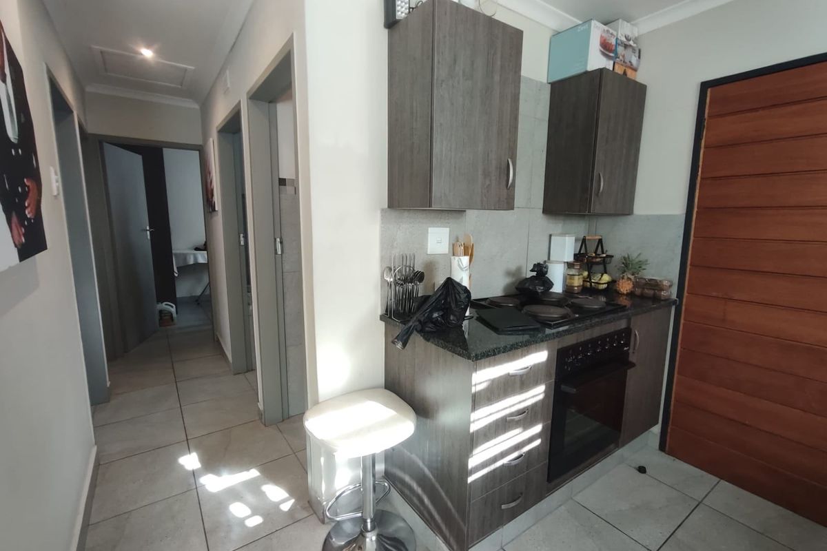 Compact kitchen area featuring modern dark wood cabinetry, granite countertops, and integrated electric oven and hob, with tiled flooring throughout.