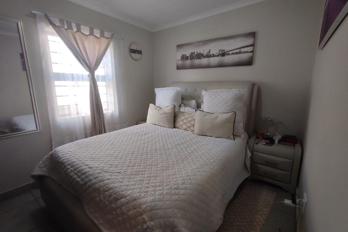 A well-maintained bedroom featuring tiled flooring, neutral wall tones, and a window fitted with security bars.
